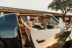 Vintage convertible car at sunset with a golden glow, parked outside a brick building with string lights.