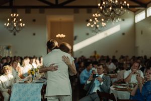 Reception guests watch couple sharing first dance under elegant chandeliers in an airy venue.