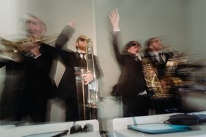 Motion-blurred photo of musicians performing in formal attire with raised instruments.