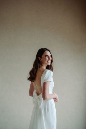 An elegant white wedding dress with short puffed sleeves and an open back design is shown against a neutral background.