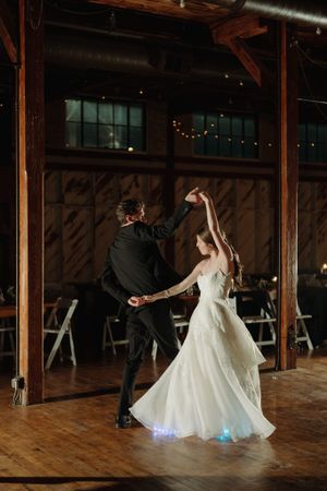 A couple dances together in an elegant wedding venue with wood beams and twinkle lights at their first dance.