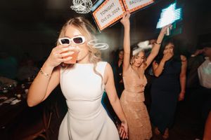 Partygoers in sunglasses and formal dresses dancing and celebrating at a nighttime event.