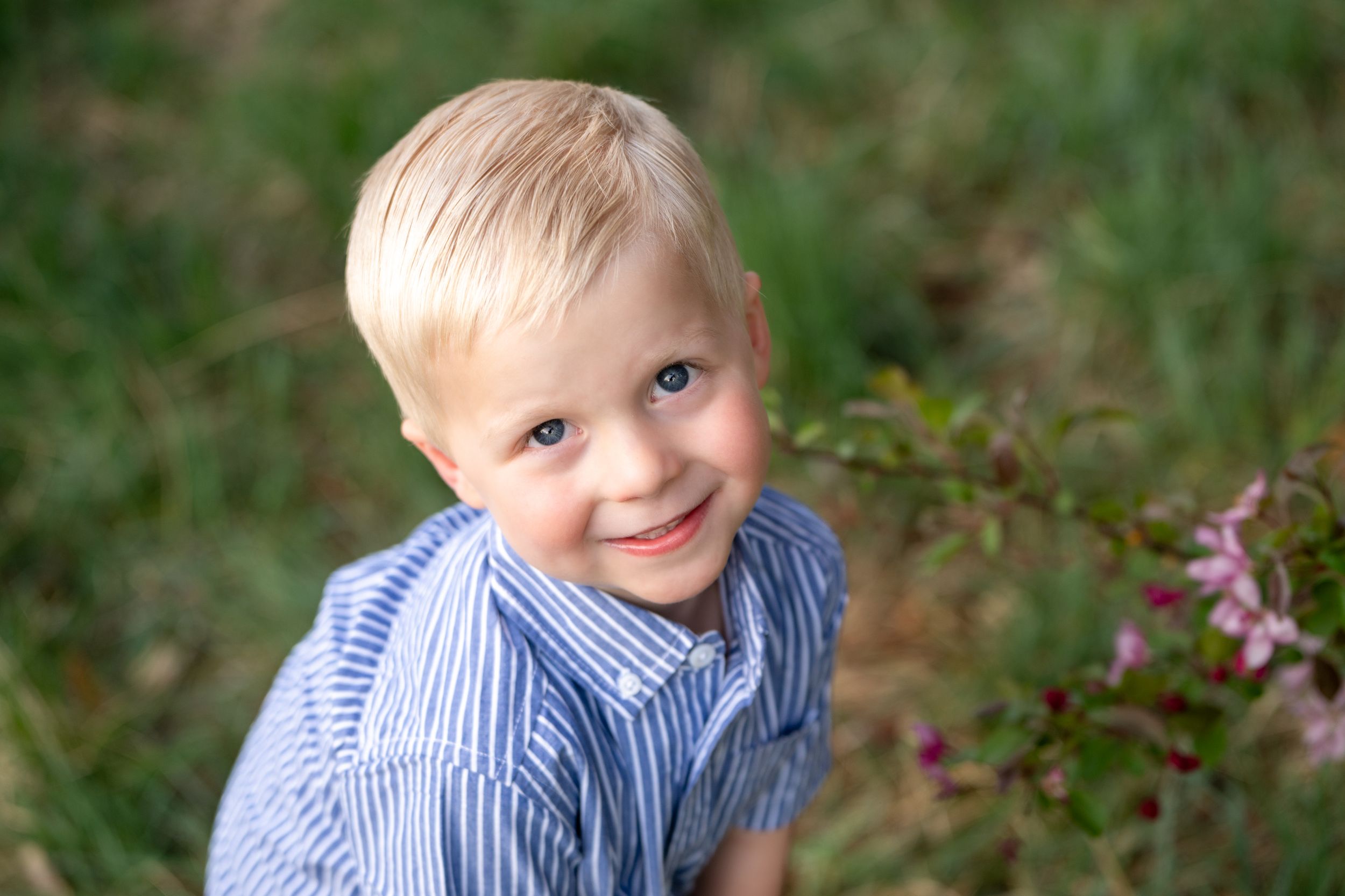 A child in a blue striped shirt smiles while playing outdoors in a grassy area.