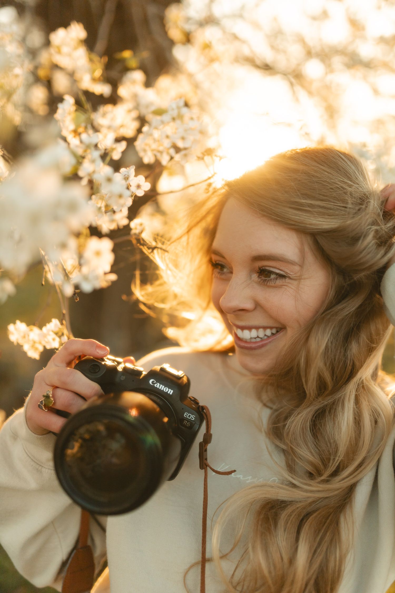 kansas city newborn photographer smiling with her canon camera surrounded by white blooming flowers in the spring