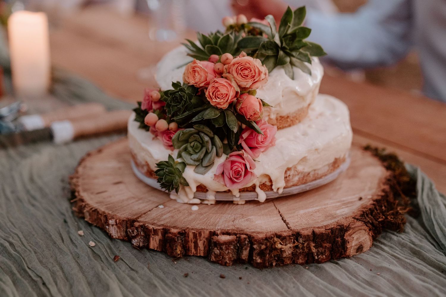 Elegant naked wedding cake topped with pink roses and succulents on a rustic wood slice.