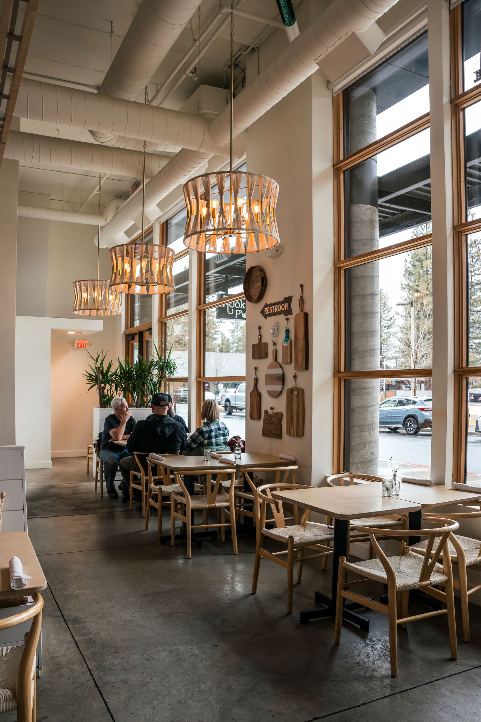 Modern cafe interior with wooden furniture, stylish pendant lights, and large windows creating a bright, welcoming atmosphere.