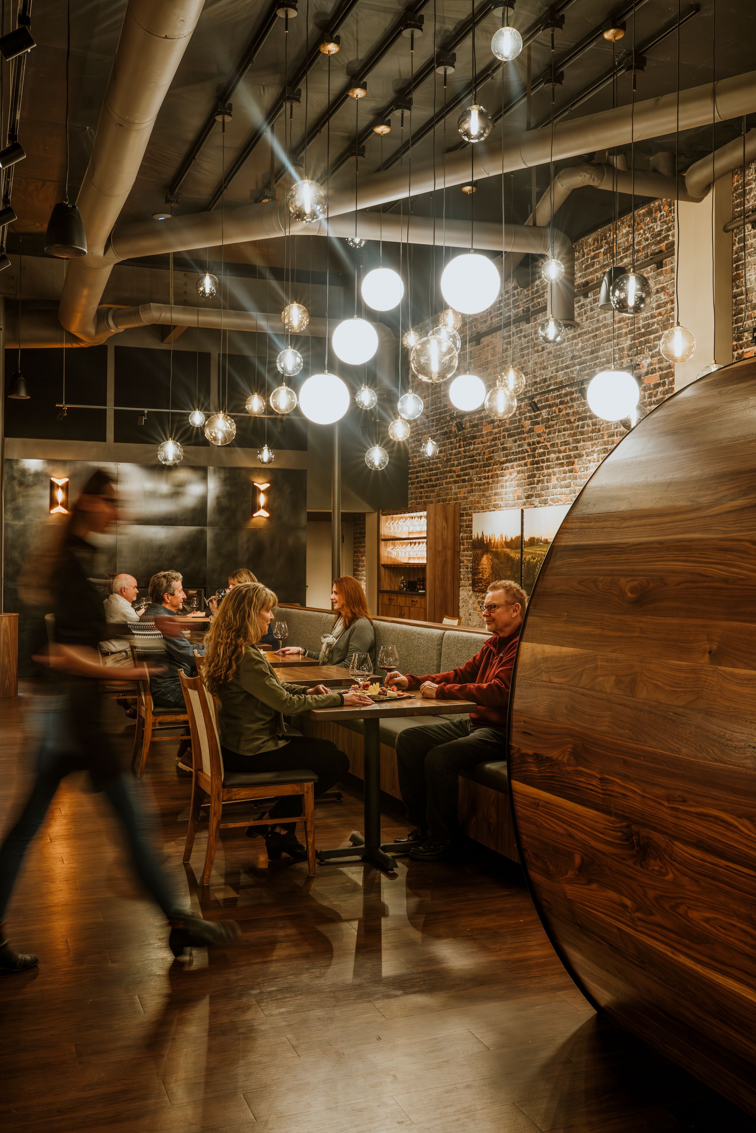 A cozy restaurant interior with hanging globe lights, exposed brick walls, and wooden booth seating creates warm ambiance.