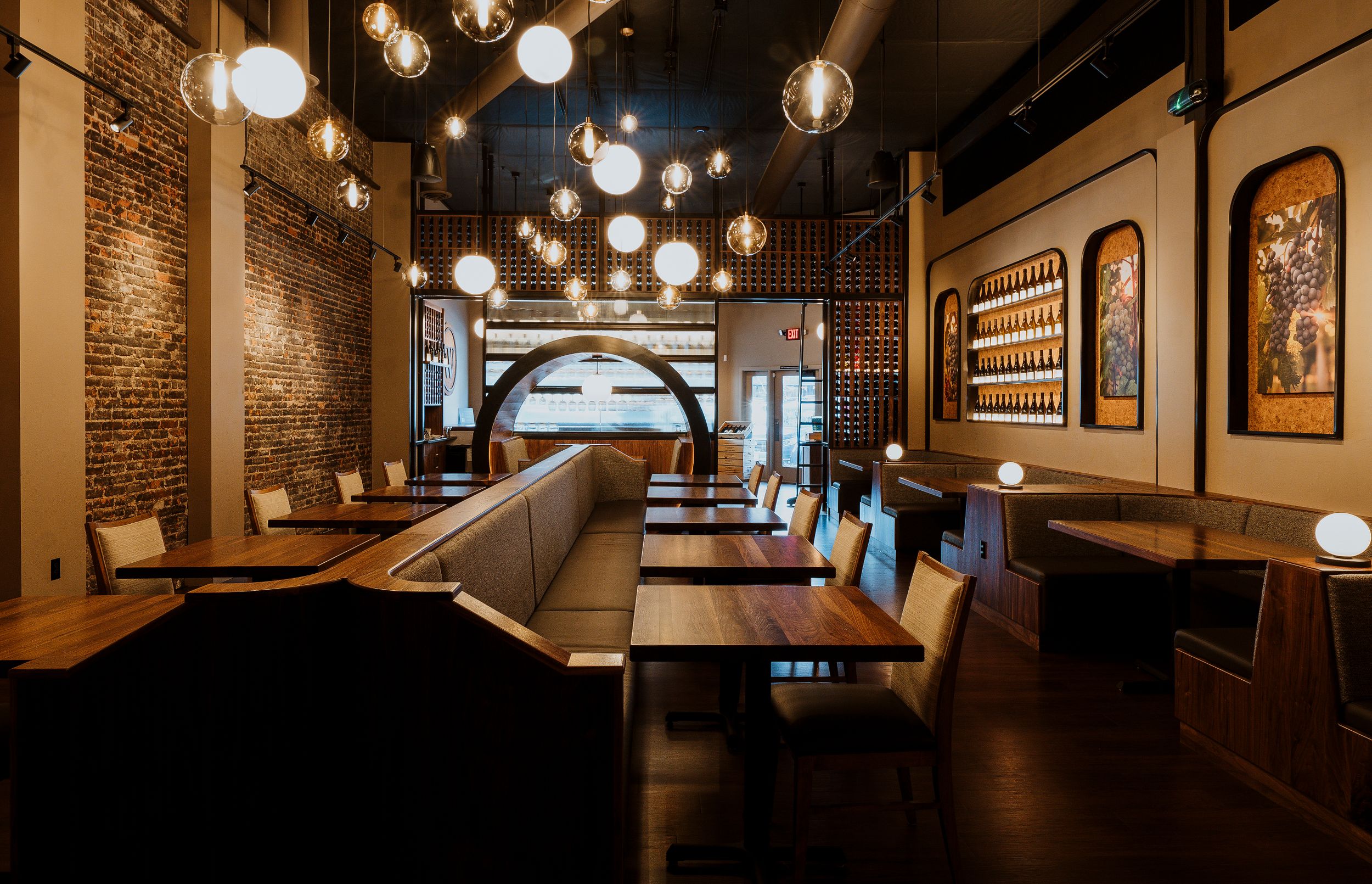 Modern restaurant interior with exposed brick walls, hanging globe lights, and leather booth seating in warm ambient lighting.