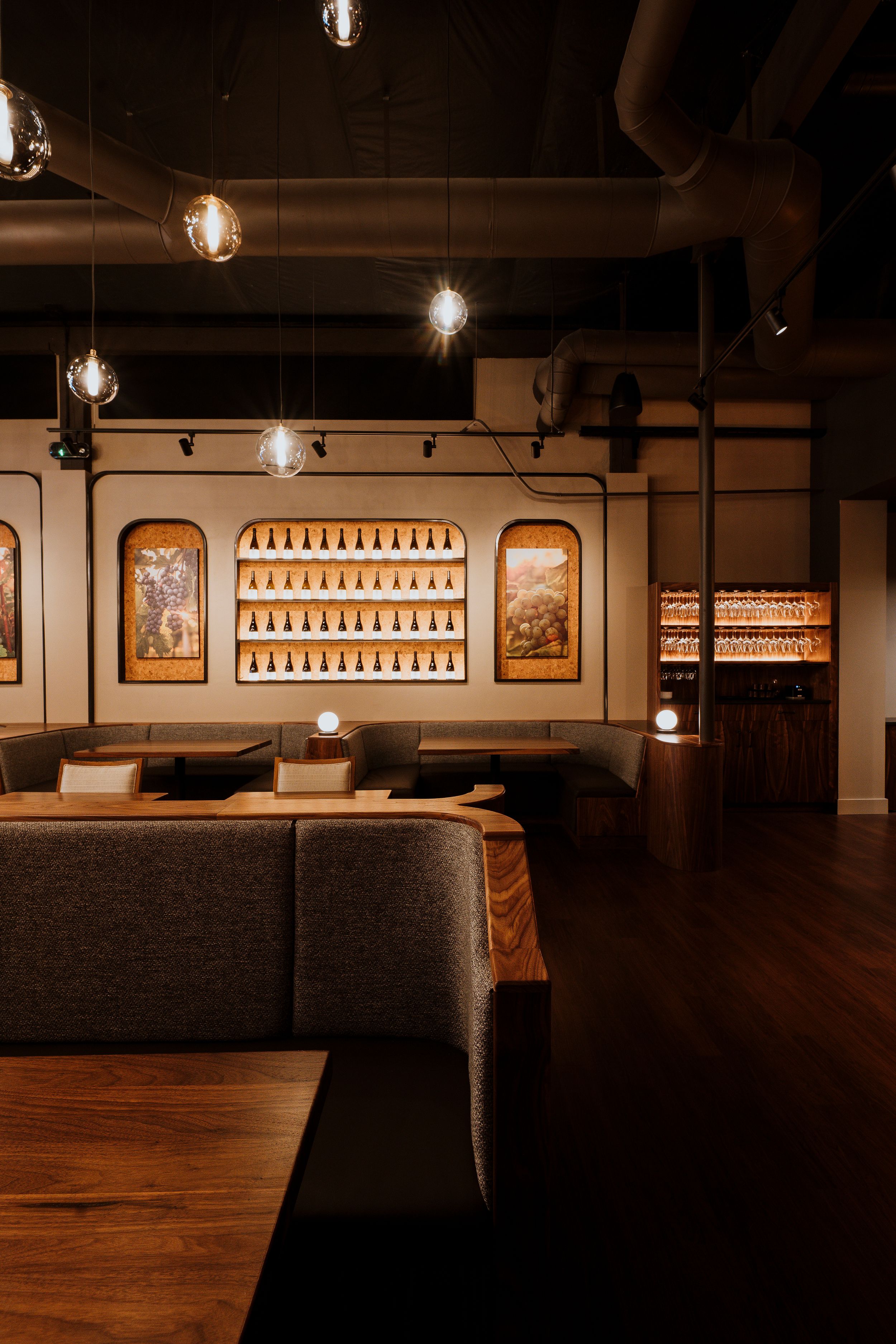 Cozy restaurant interior with warm lighting, gray booth seating, and illuminated bottle displays on wooden walls.