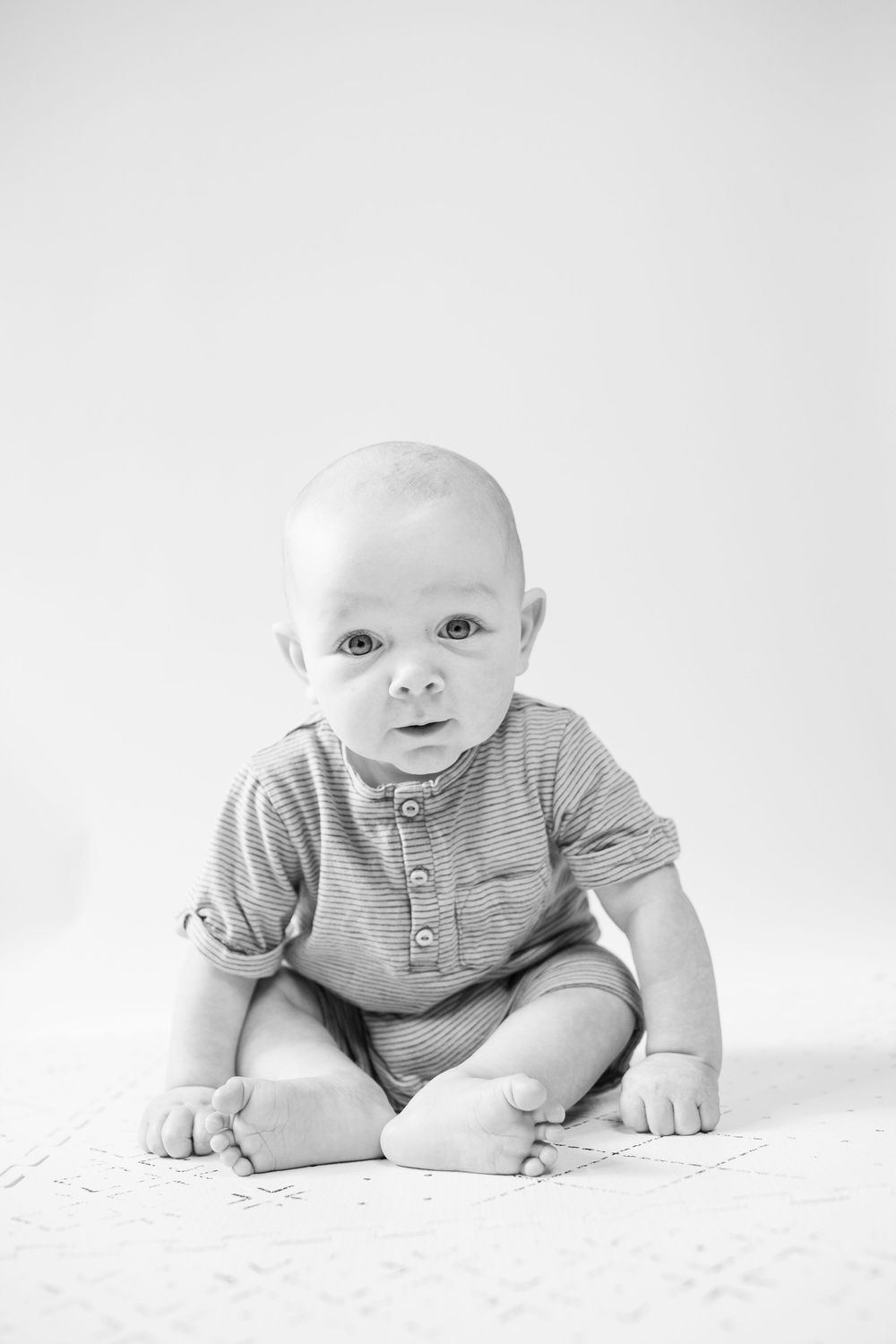 Black and white portrait series of an infant in gray clothing lying on white fabric.