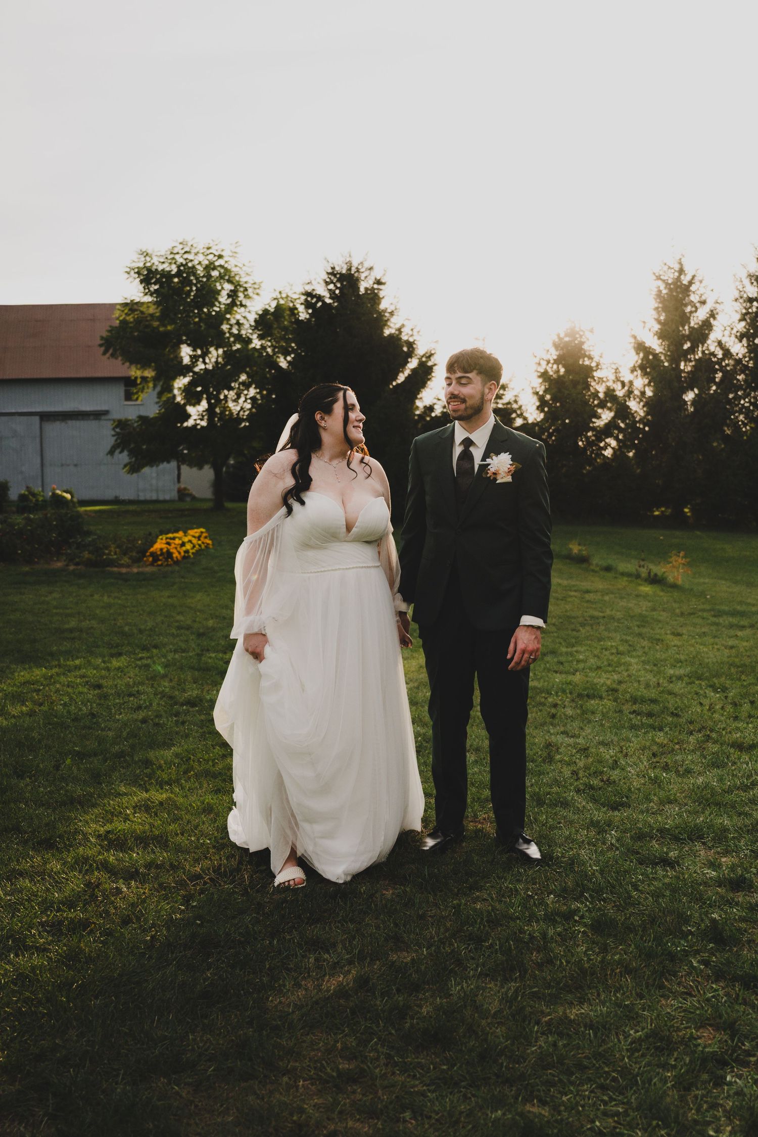 A couple walks hand in hand along a scenic beach shoreline in formal wedding attire.