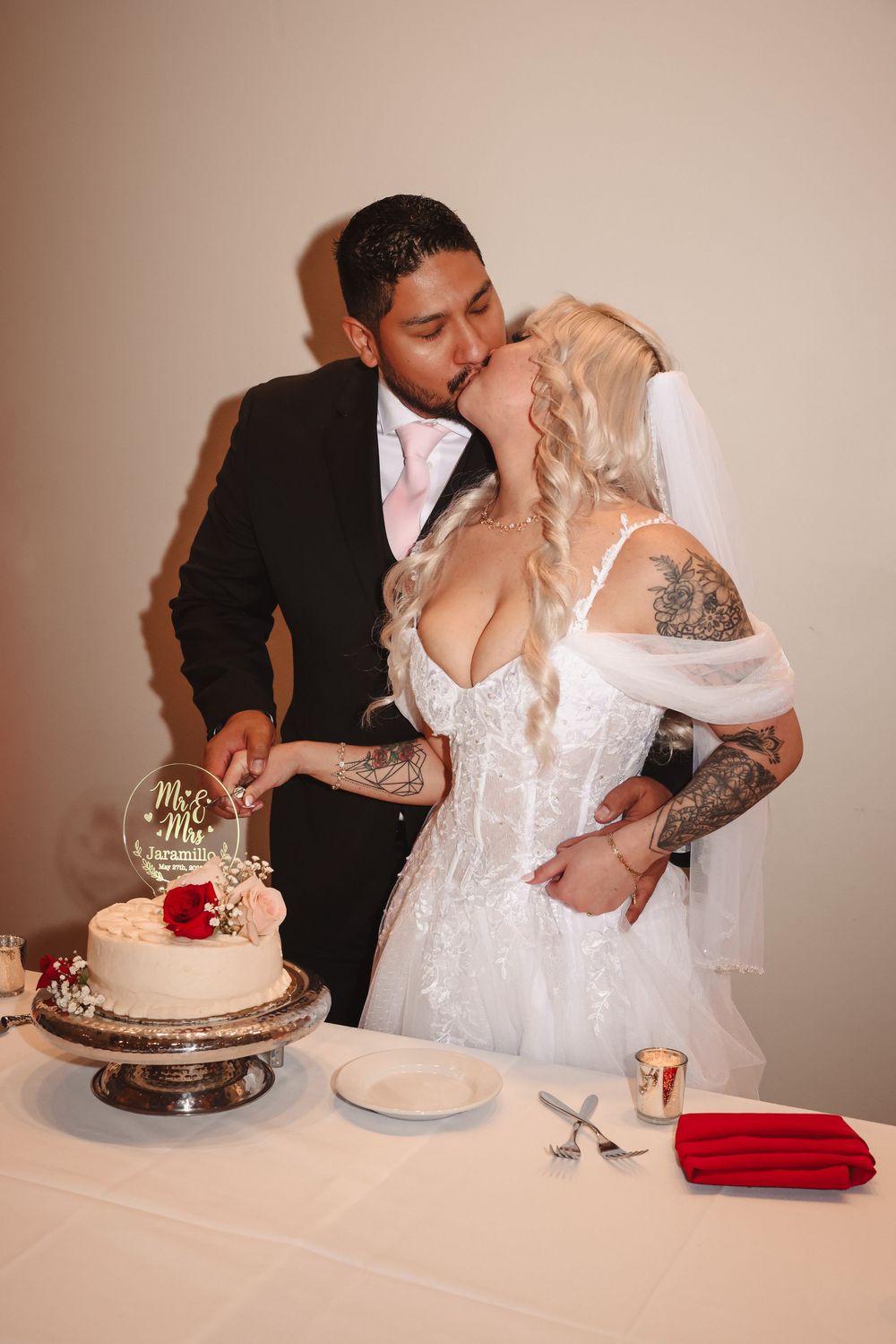 A bride and groom share a kiss while cutting their wedding cake at the reception.
