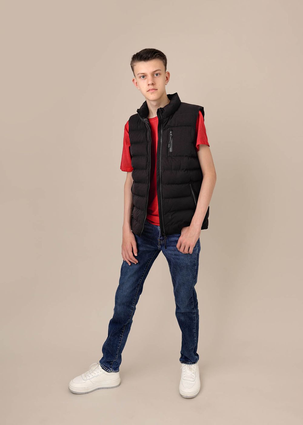 Teenage boy standing in a confident model pose wearing jeans and a red t shirt in a photography studio
