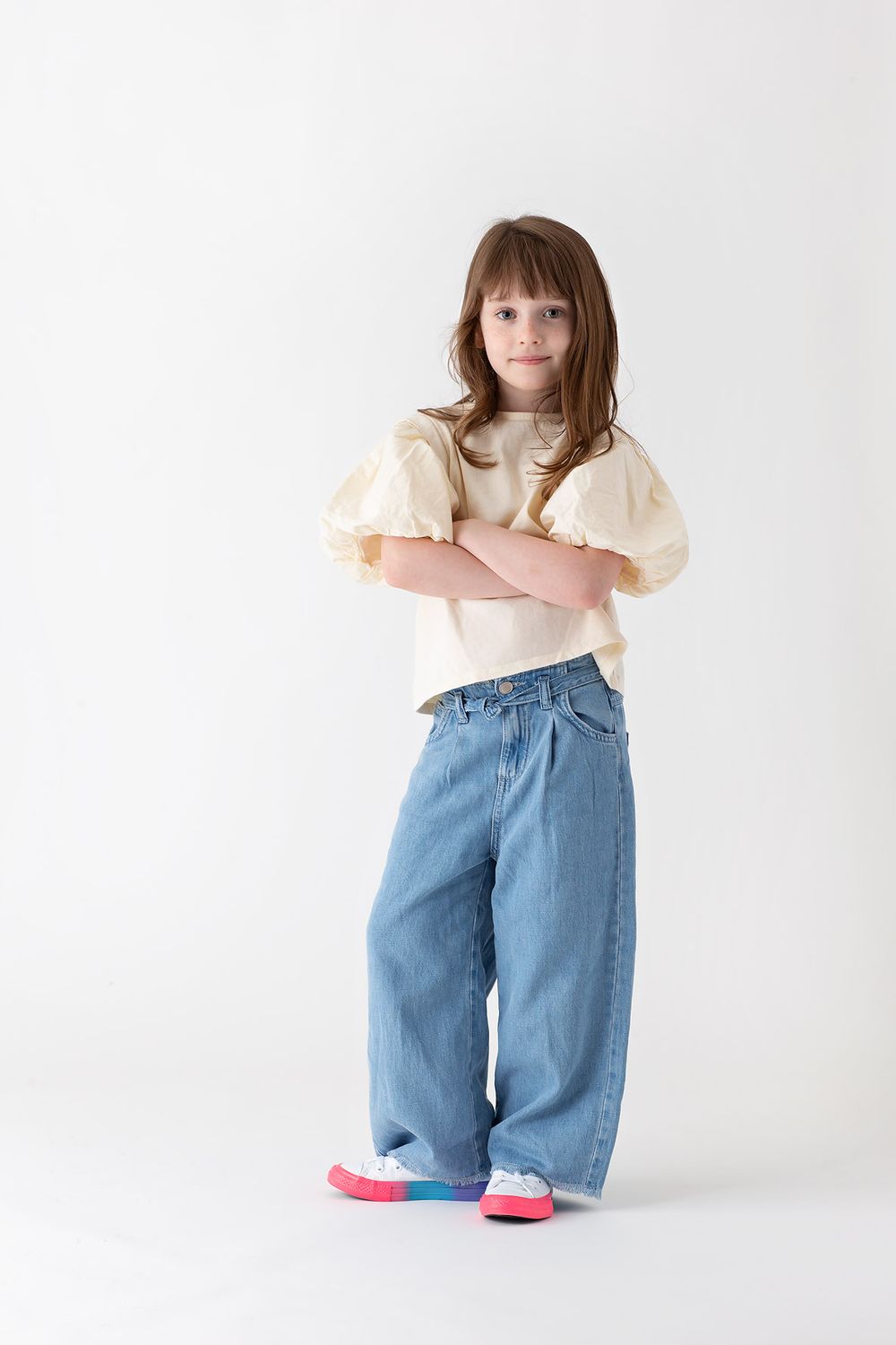 Young girl fashion portfolio wearing pink top and baggy blue jeans with red shoes for commercial shoot