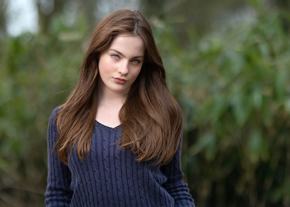 Teenage model with flowing auburn hair in navy cable knit sweater during natural light outdoor photoshoot