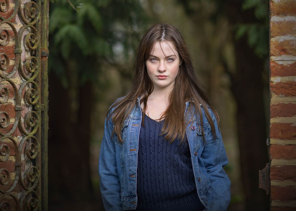 Young woman model in denim jacket and navy top for fashion portfolio shoot with brick archway background