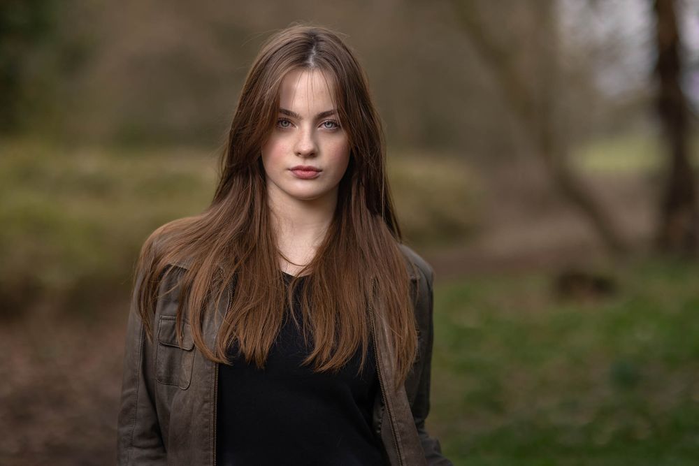 Young actress in khaki jacket and black top for outdoor headshot session with natural woodland backdrop