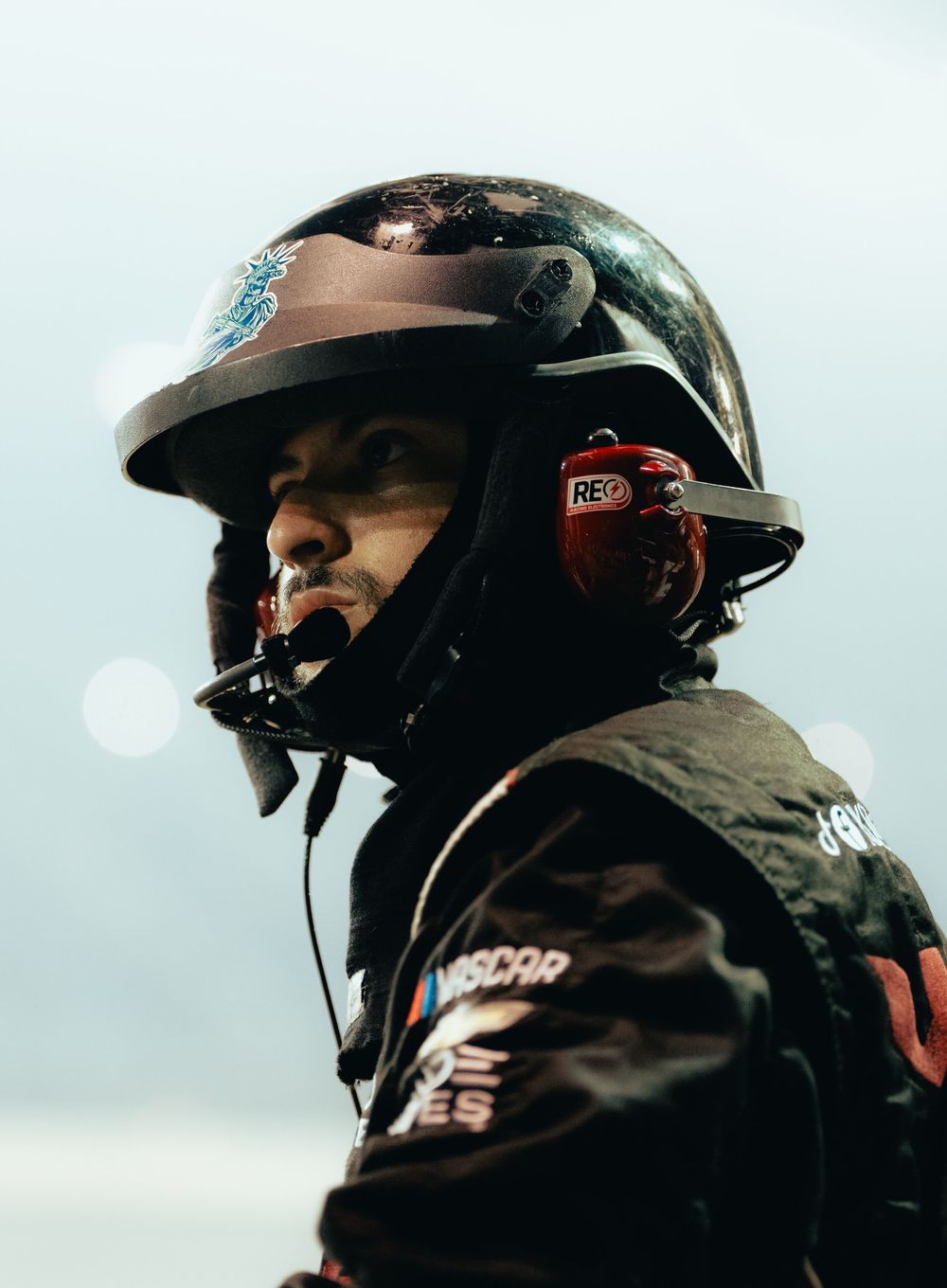 NASCAR pit crew member wearing a dirty helmet and radio headset, focused during a race event.
