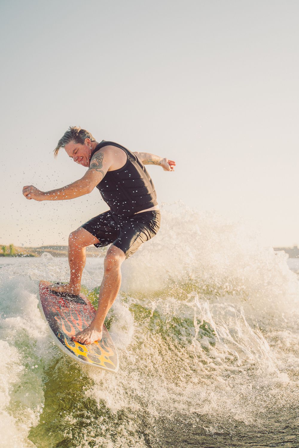 Wakeboarder creating dramatic splashes while riding waves on a sunny day.