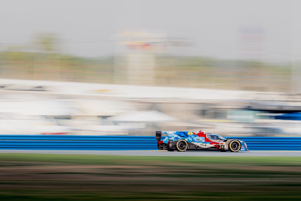 A blue racing car speeds along a track with motion blur background at a professional motorsport event.