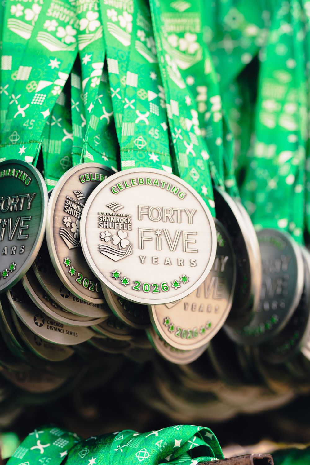 Closeup of multiple silver sobriety recovery medallions hanging against a green background with text visible on their surfaces.