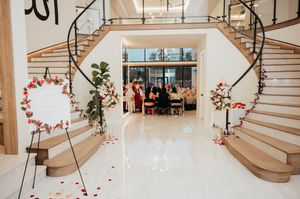 Modern wedding venue interior with curved wooden staircase and scattered red rose petals on white floor.