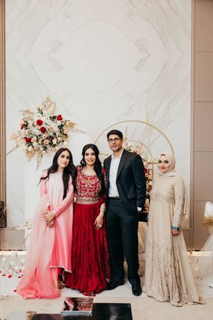Group photo at a formal event with people wearing elegant gowns in pink, red, and cream colors against a marble backdrop.