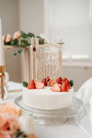 Elegant white birthday cake decorated with fresh strawberries and gold script topper on a minimalist table setting.