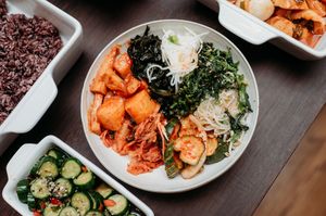 Plates of Korean food including kimchi, fresh vegetables, and garnishes arranged on a dark wooden table.