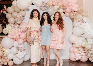 A group poses against a beautiful backdrop of pink and white balloon garlands and floral decorations at a celebration.