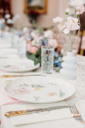 Elegant wedding table setting with delicate pink flowers, crystal glasses, and white plates with ornate designs.