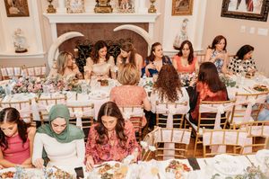 People gather at tables in a dining room for a social event with white tablecloths and decorative elements.