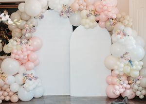 Elegant balloon arch installation in white and blush pink with floral accents against a light gray wall.