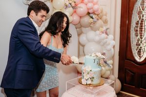 Couple cutting into their elegant light blue wedding cake at reception with pink and white balloon decor.