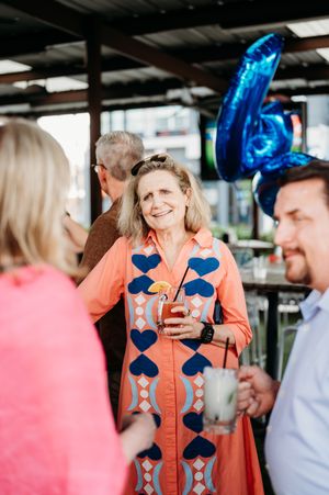 A group gathers at a party with blue balloon decorations, featuring someone in a coral dress with blue heart patterns.