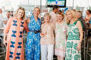 A group of women in colorful Lilly Pulitzer dresses smile and celebrate at a social gathering.