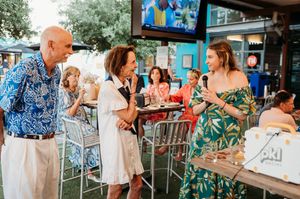 Wedding guests mingling outdoors on a patio with tropical decor and blue accents.
