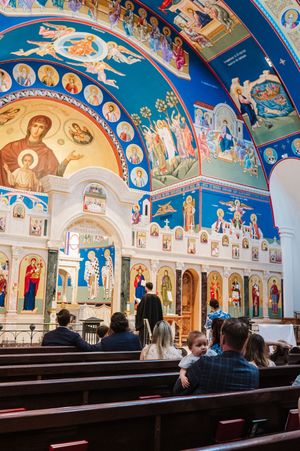 Interior view of an ornate Orthodox church with vibrant blue ceiling frescoes and wooden pews.