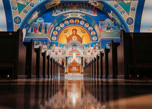 Ornate Orthodox church interior with golden iconography and rows of wooden pews leading to an illuminated altar.