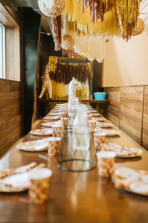 A long wooden table set for a party with gold decorations and metallic fringe hanging from the ceiling.