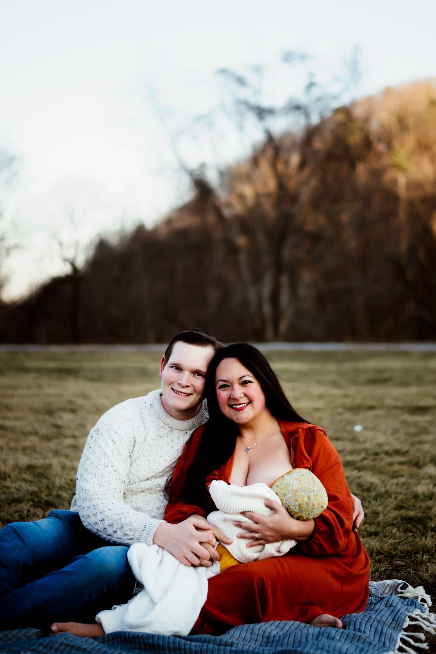 Mom nurses baby while dad holds her and they smile together at the camera