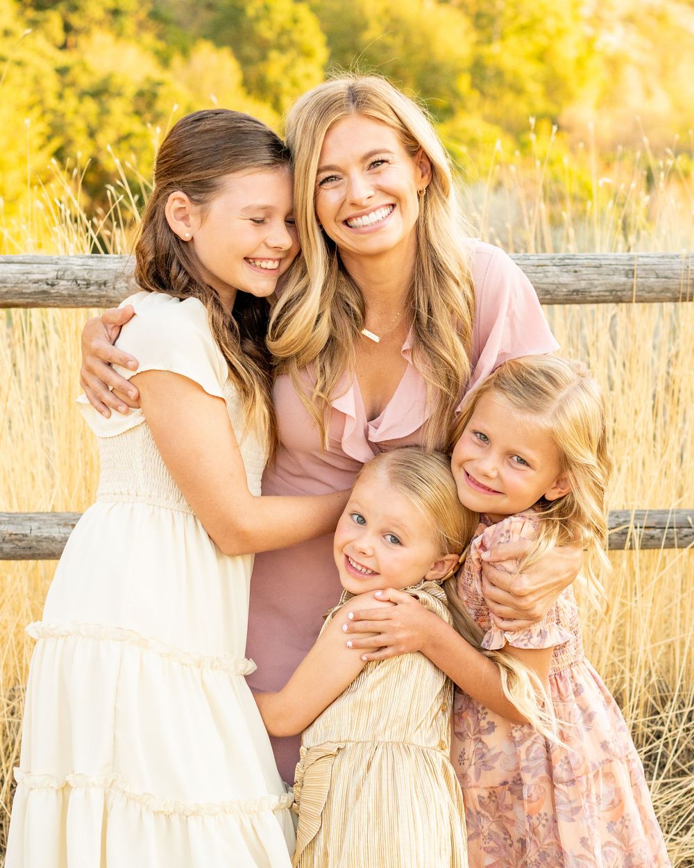 A sunlit family portrait in a golden field with rustic wooden fence at Hidden Valley Park.
