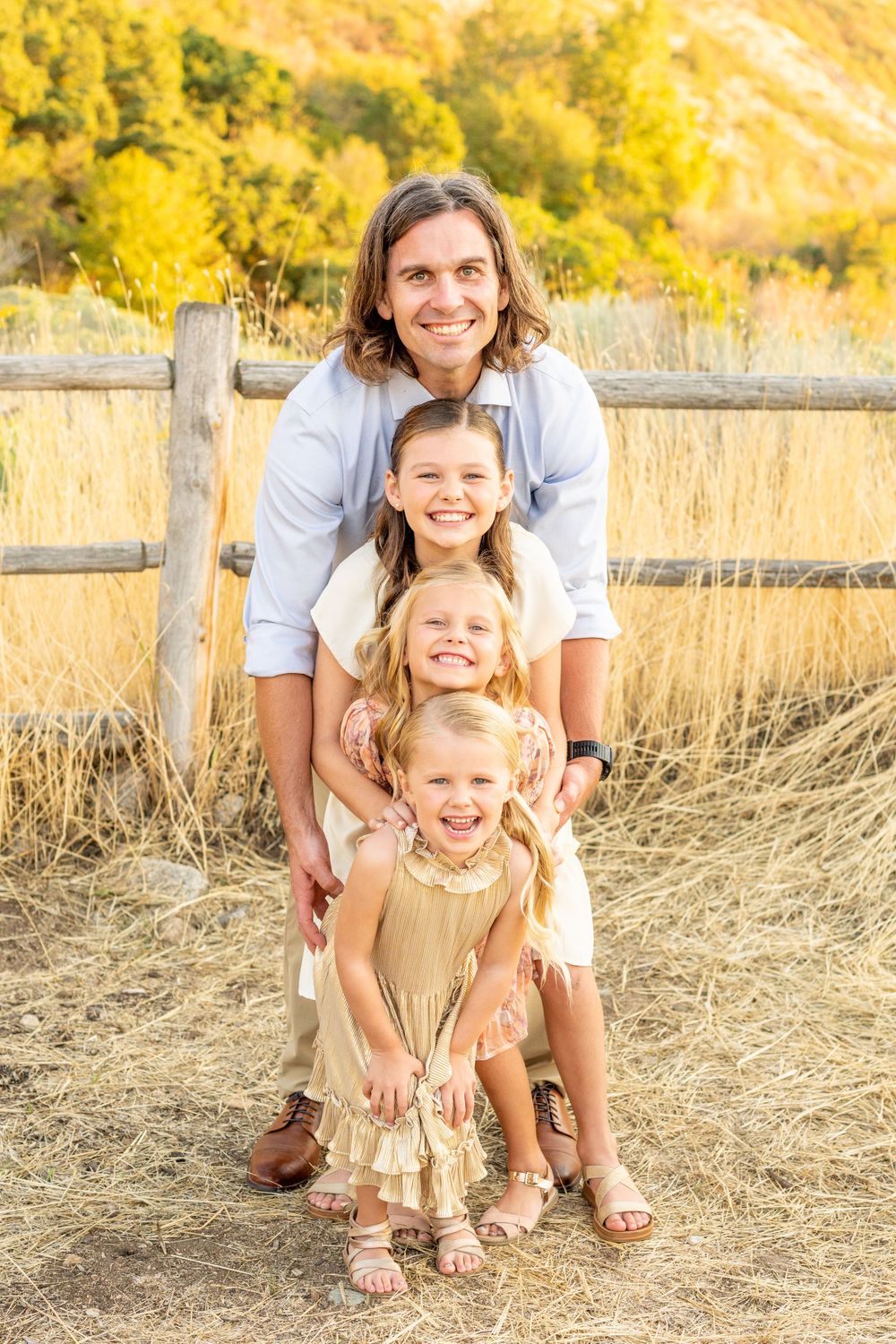 A family poses together in golden sunlit field with wooden fence and autumn foliage in background at Hidden Valley Park.