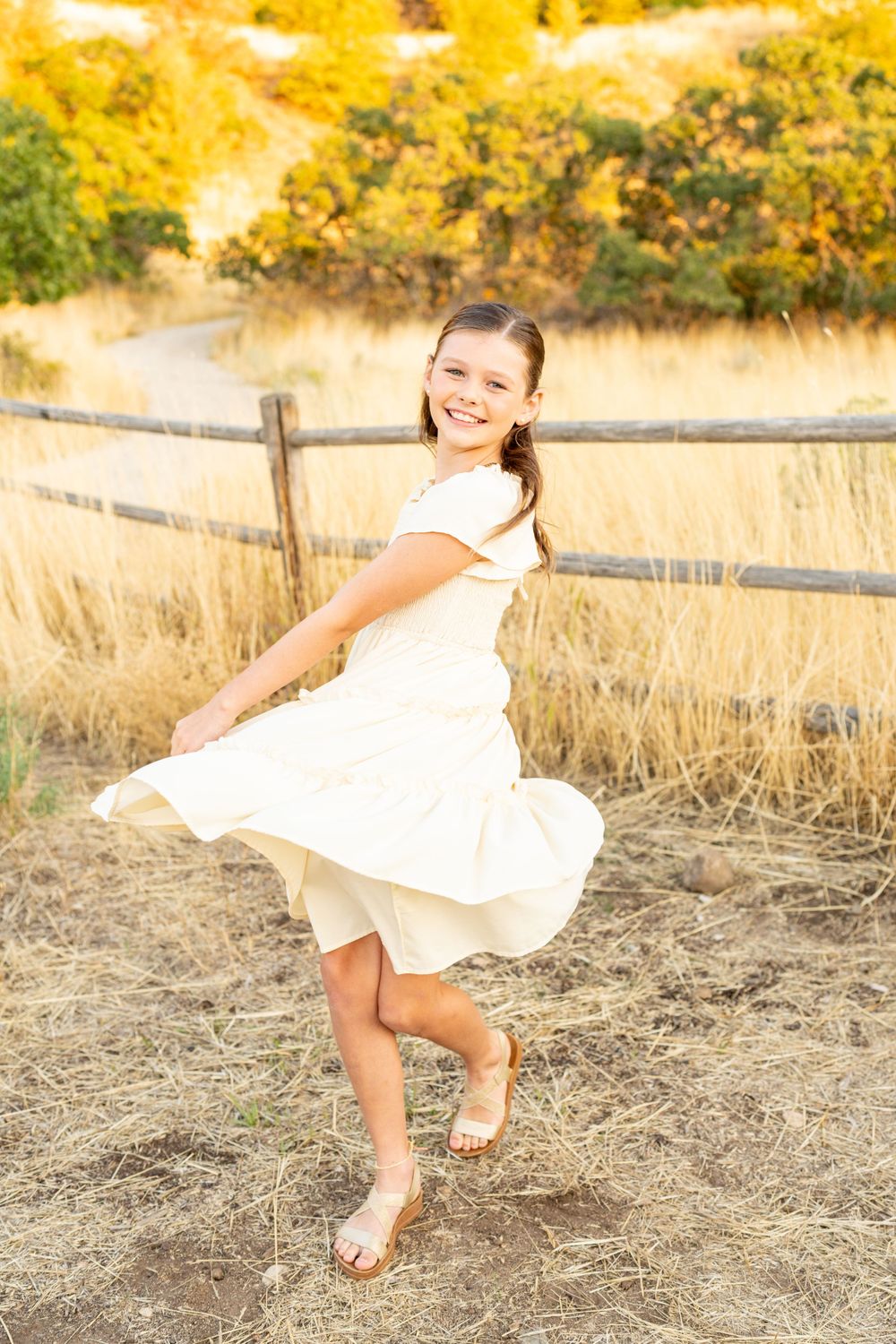 Dancing in a white dress against golden autumn field and wooden fence at Hidden Valley Park.