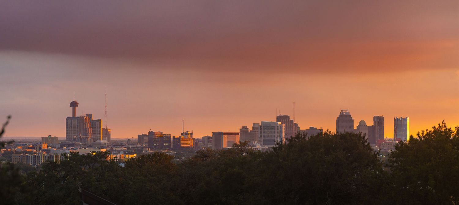 Dramatic sunset illuminates a cityscape silhouette with vibrant orange and purple hues in the sky.