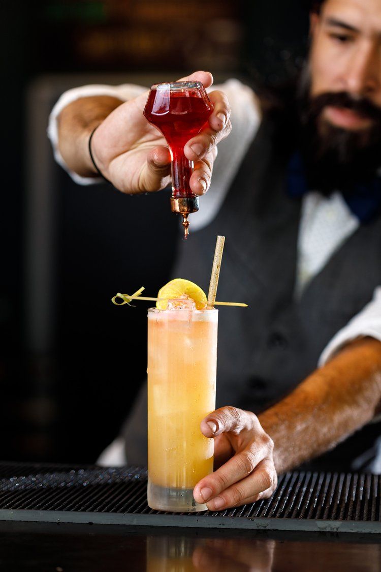 Orange cocktail garnished with lemon peel getting a red wine float added as final touch.