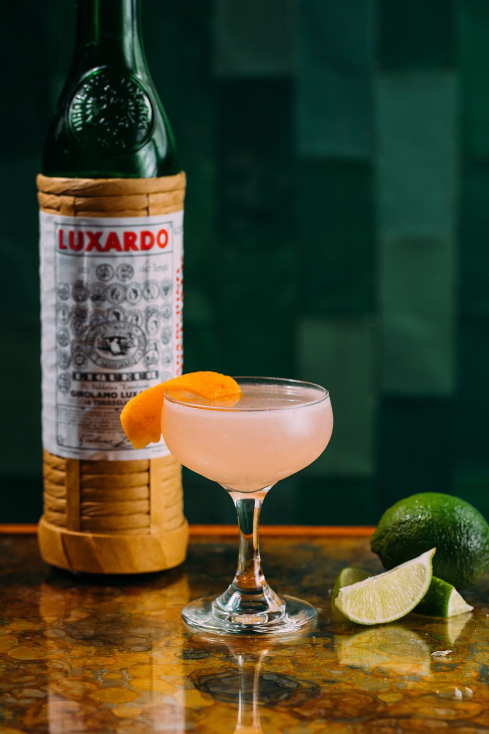 Bottle of cocktail mix with a prepared drink and garnish on a bar counter