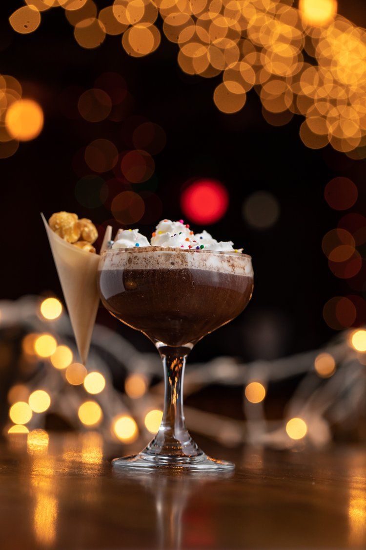 Elegant dessert cocktails with whipped cream garnish against a bokeh light background.