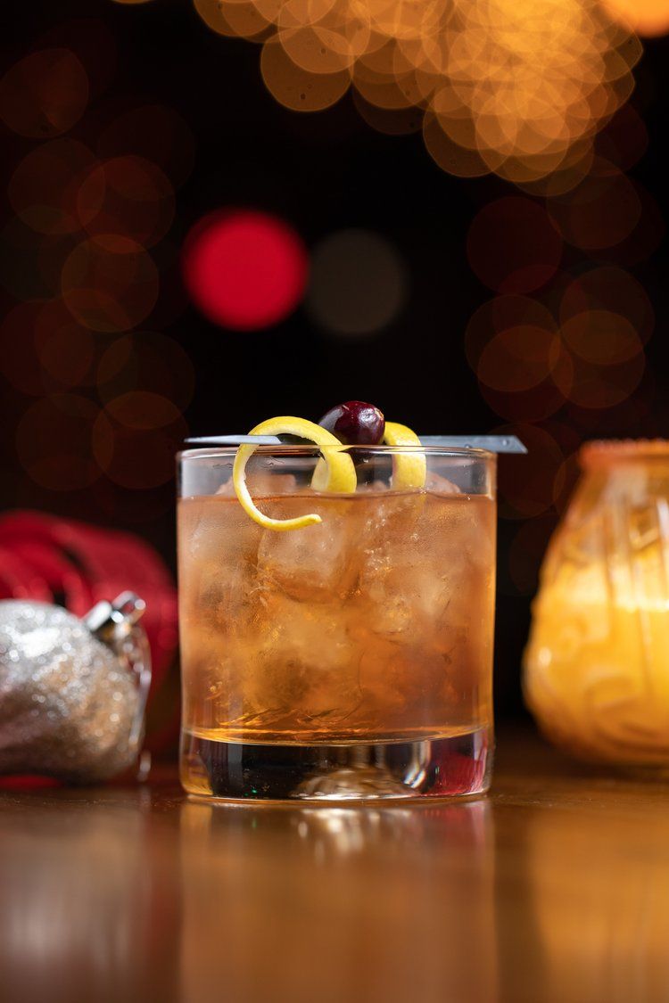 Classic cocktails with citrus garnish on a dark bar with ambient lighting and bokeh effects.