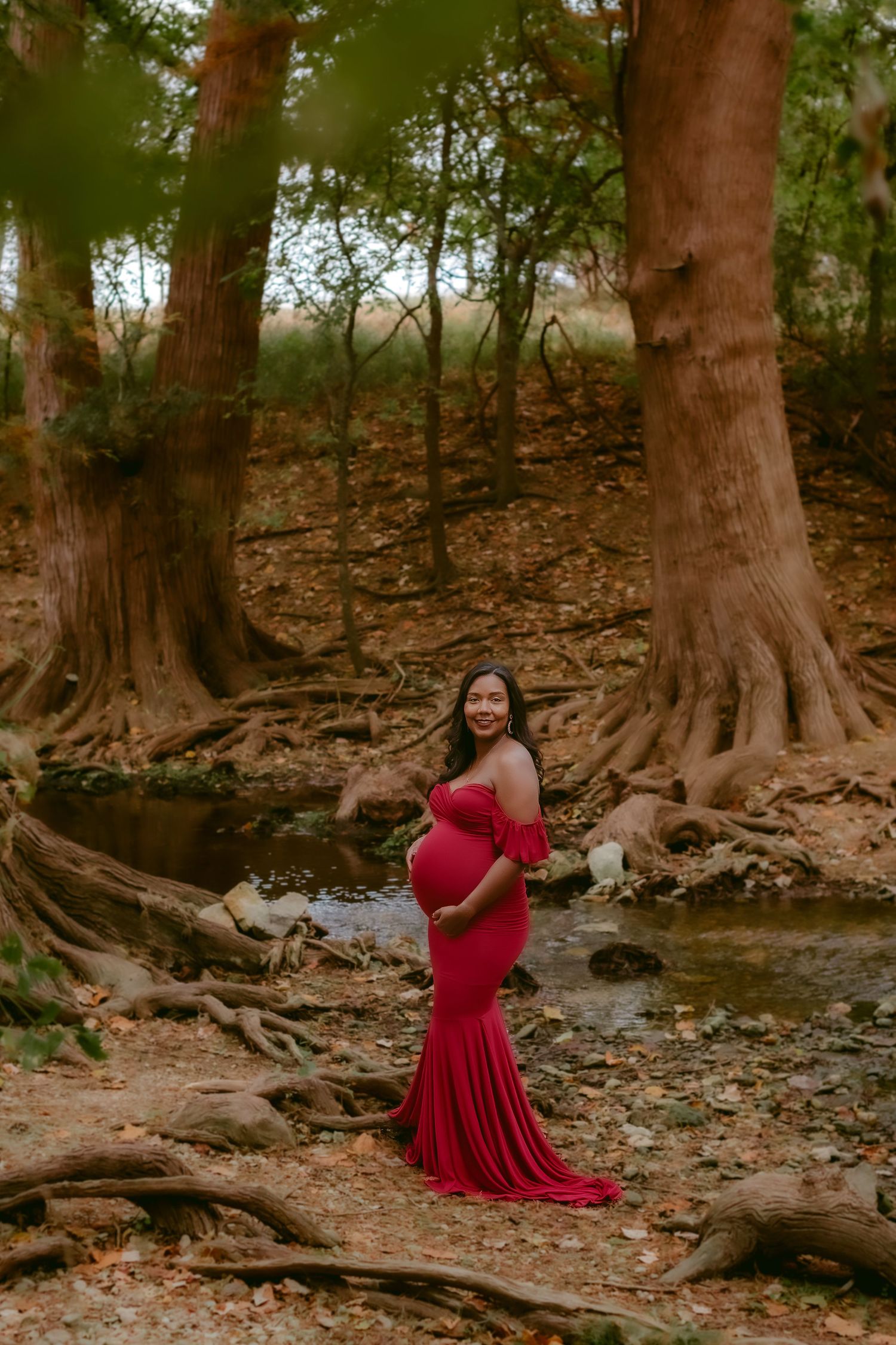 A red dress stands out against exposed tree roots and fallen leaves in a moody forest setting.